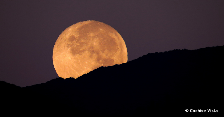Supermoon raising over hills on a clear dark night.
